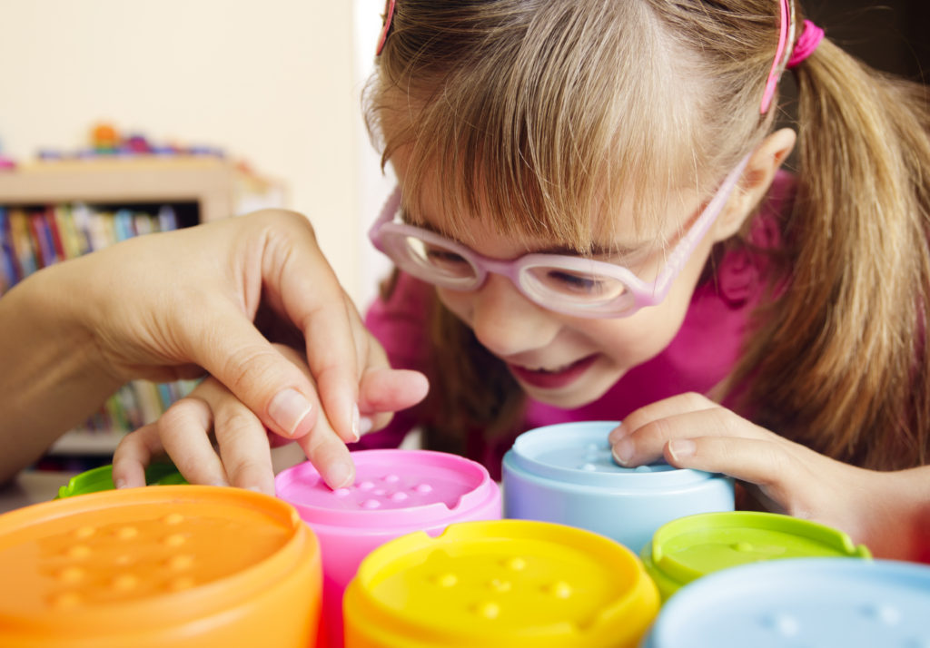 Little girl with poor vision is playing with colorful tactile toy cups as a part of occupational therapy with her teacher.